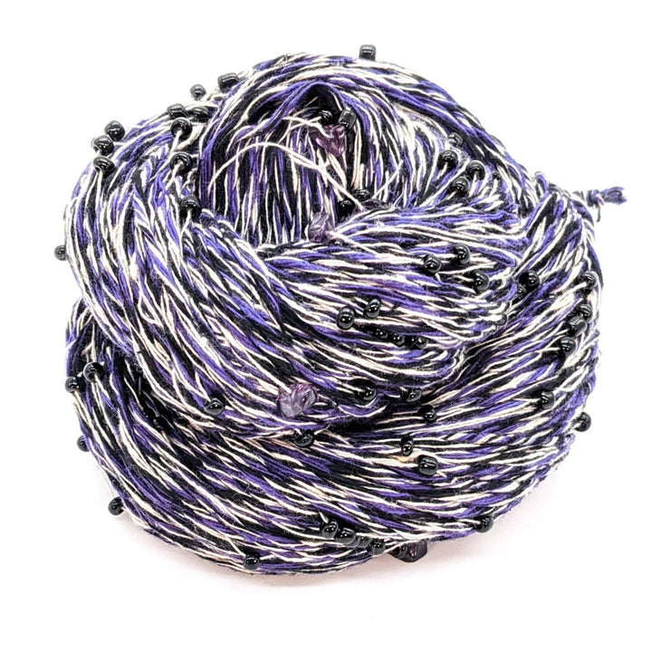 Skein of multicolored yarn in purple, white, and black with small black beads.