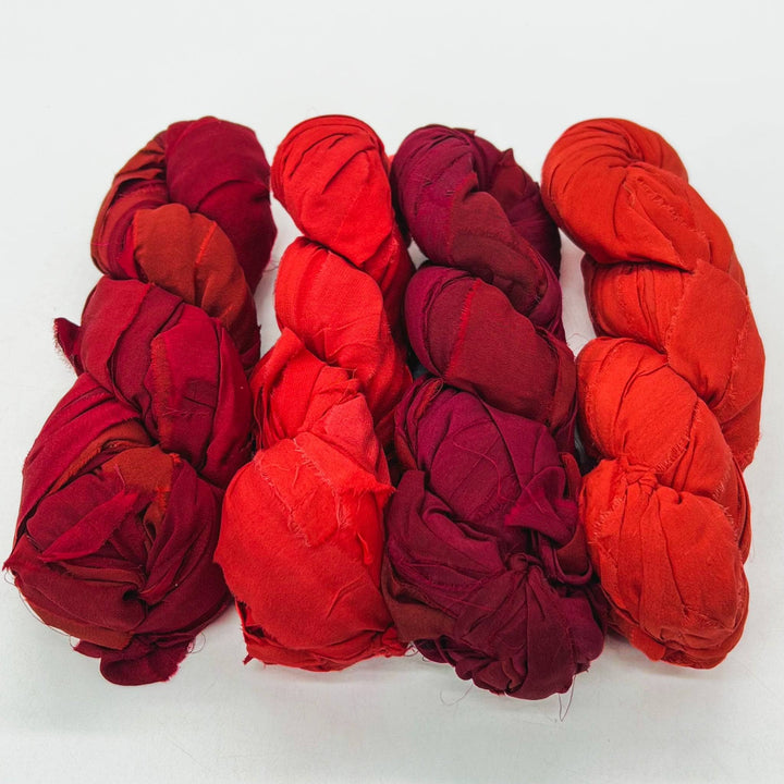 Five twisted fabric bundles in red and orange laid side by side on a white background.