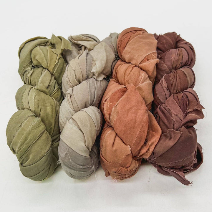 Five fabric bundles in green, beige, orange, and brown, wrapped on a white surface.