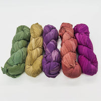 Five rolled fabric bundles in green, yellow, purple, red, and magenta lined up side by side.