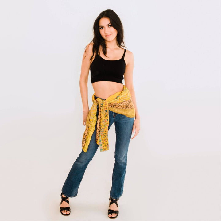 A woman posing in jeans and a yellow wrap tied around her waist.