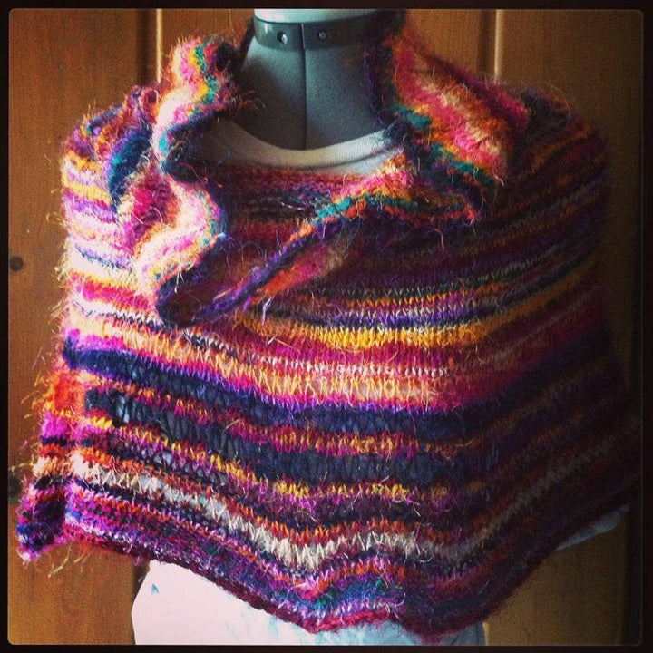 Mannequin wearing a multicolored striped knit shawl and standing in front of a wooden wall 