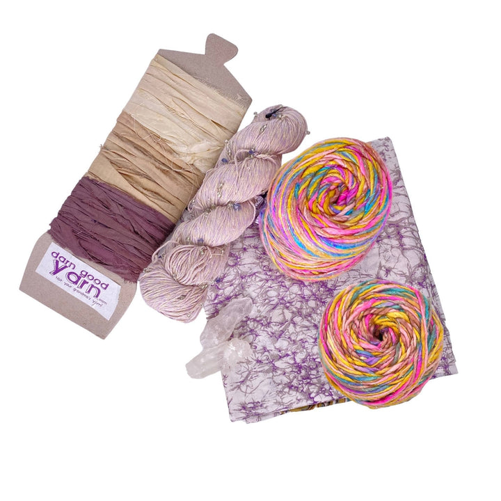Mystical Clear Quartz energy bundle with all items showing in front of a white background. 2 clear quartz crystals, 2 skeins sparkle worsted weight silk, 1 skeins chakra beaded cotton yarn, 3 color sari silk ribbon sample card, and coordinating furoshiki.