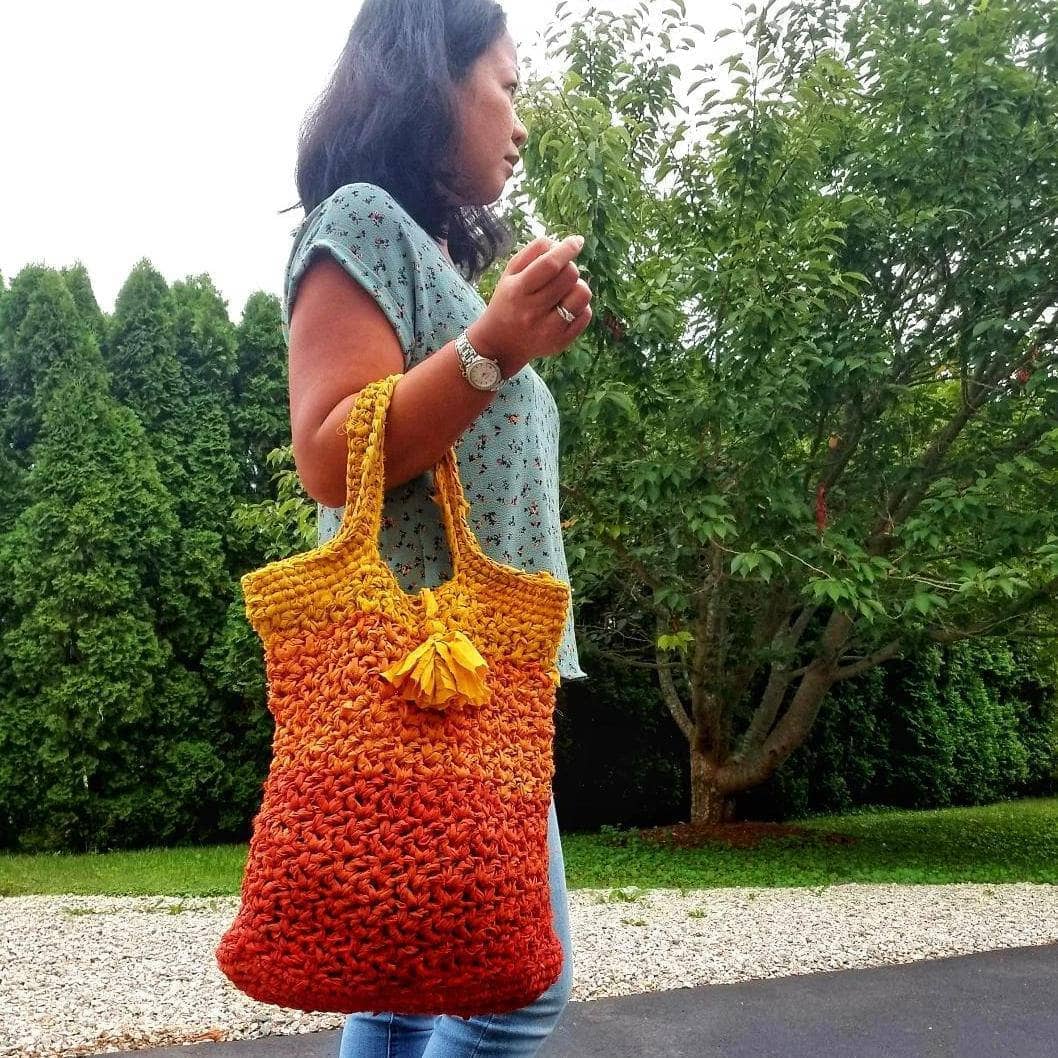 A woman holding a orange ombre tote bag outside 