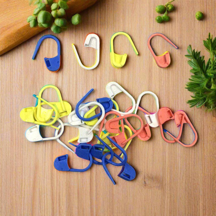 Pink, blue, yellow, and white knit stitch markers strewn on a white background