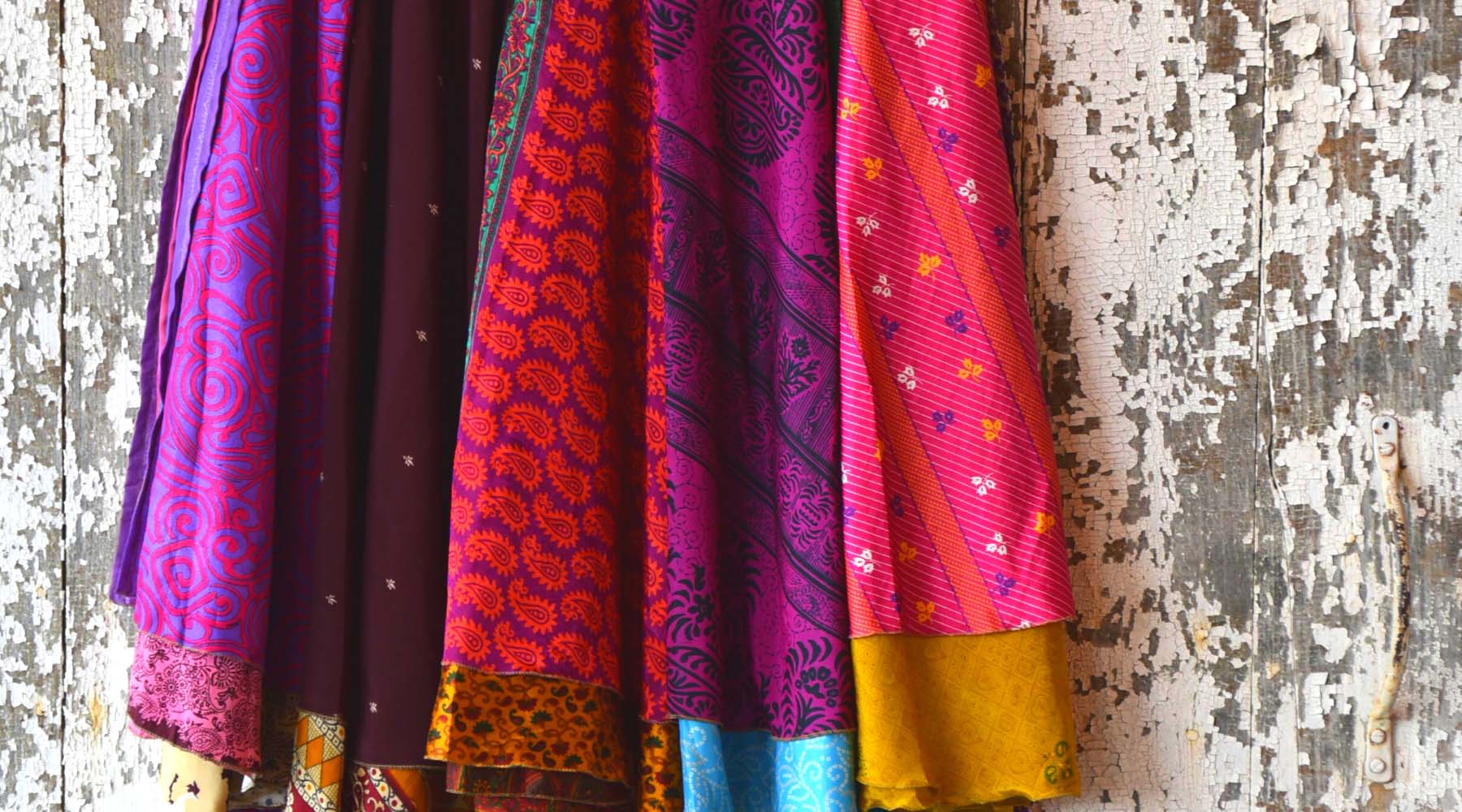 Five brightly colored sari wrap skirts hung against weathered painted wood wall 