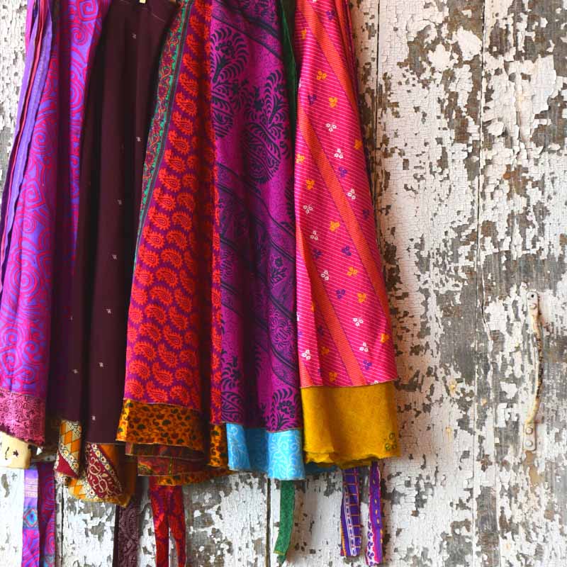 Five brightly colored sari wrap skirts hung against weathered painted wood wall 
