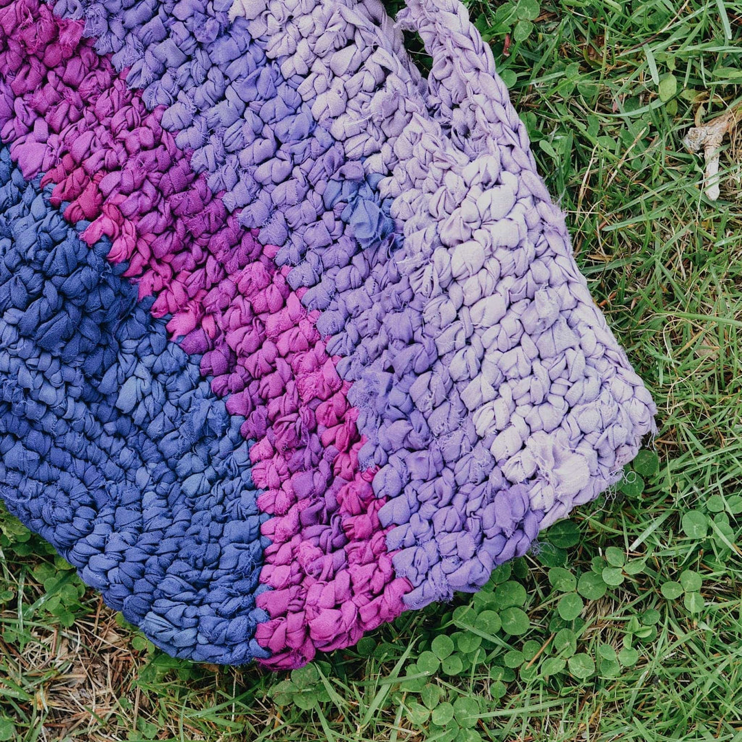 Crochet version of purple tonal recycled chiffon market bag with greenery in the background.