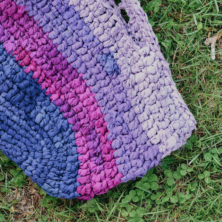 Crochet version of purple tonal recycled chiffon market bag with greenery in the background.