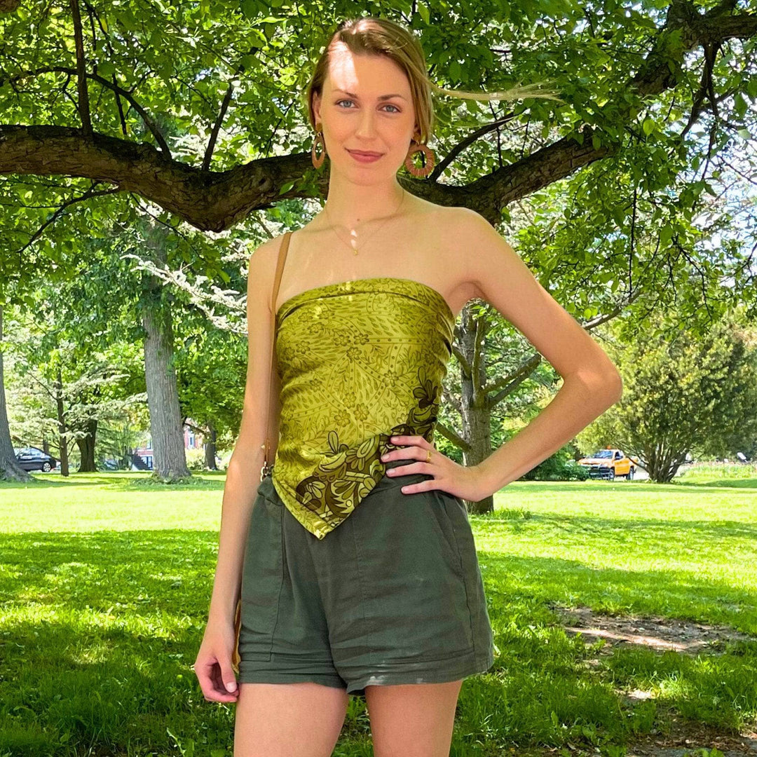 A woman outdoors wearing a green patterned top and green shorts under a tree.
