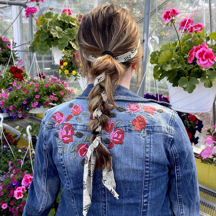 A girl standing in a flower shop white a white & black sari bandana braided into her hair.