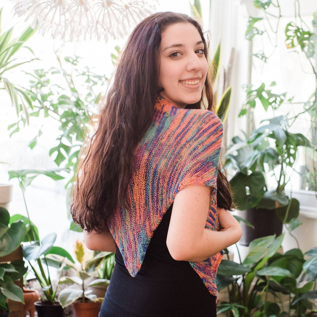 Back view of Model wearing hand beaded silk shawl knit kit in party with potted greenery in the background.