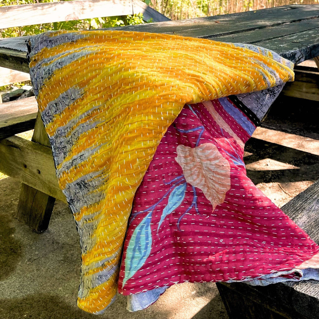 Vibrant kantha quilt draped over a wooden bench.