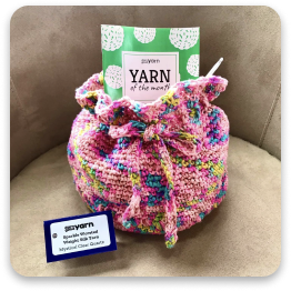 Pink and colorful crocheted bag with yarn and knitting kit inside.