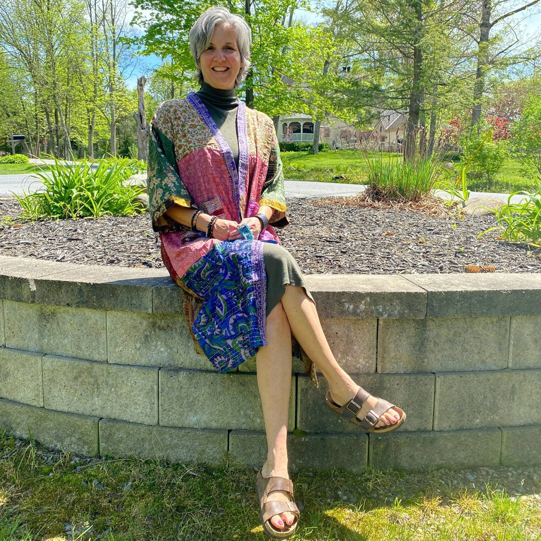 Model is sitting on a cement wall outside  wearing a one of a kind kantha jacket. 