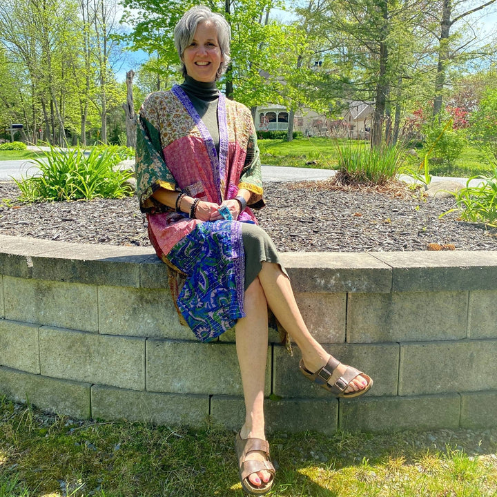 Model is sitting on a cement wall outside  wearing a one of a kind kantha jacket. 