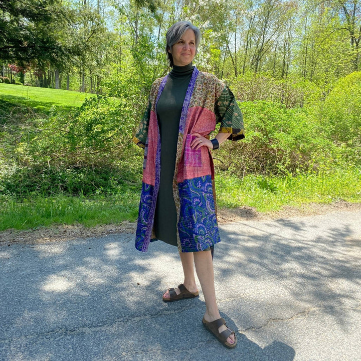 Model is standing outside wearing a one of a kind pink, blue and green kantha jacket. 