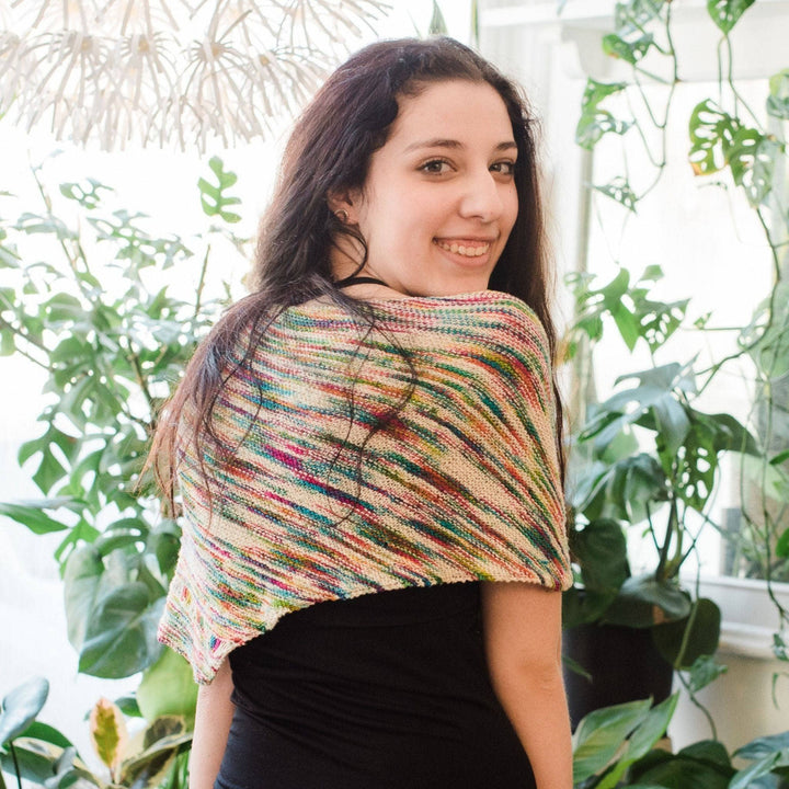 Model wearing unicorn cloud neon pop shawl with potted greenery in the background. 