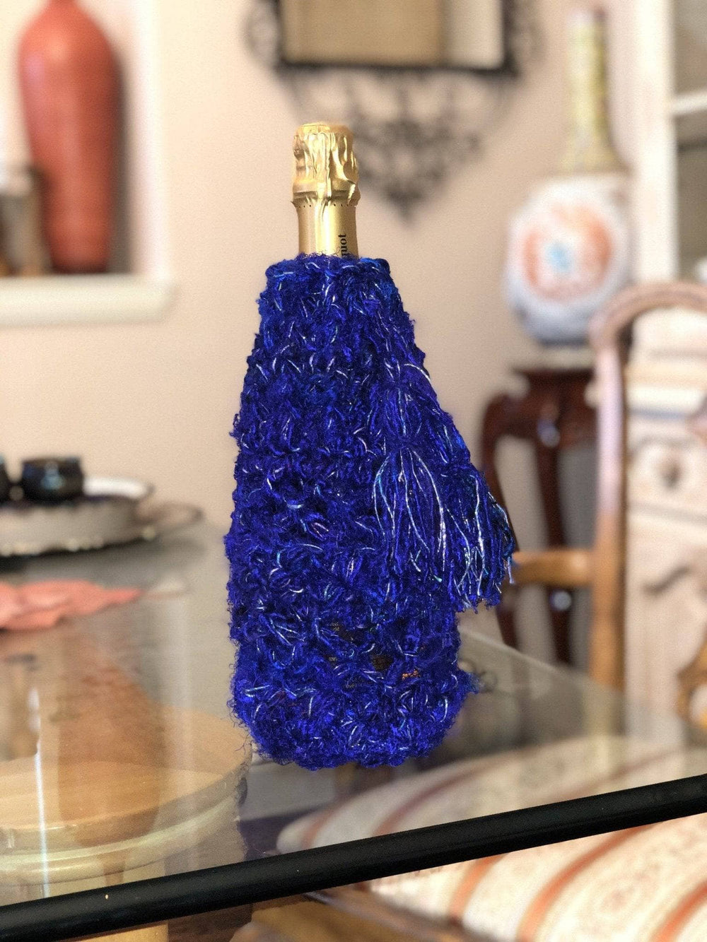 Champagne bottle wrapped in purple recycled silk on glass desk in front of blurry domestic setting
