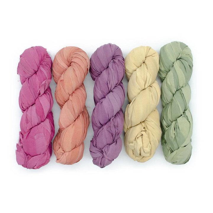 pink, orange, purple, yellow, and green chiffon ribbon yarn in front of a white background.