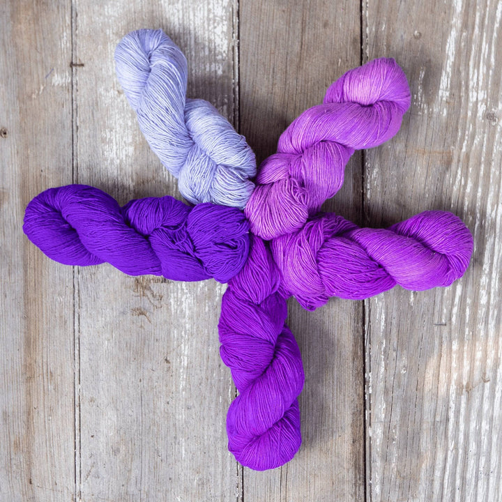  Skeins of purple and lavender yarn arranged in a star shape on wood.