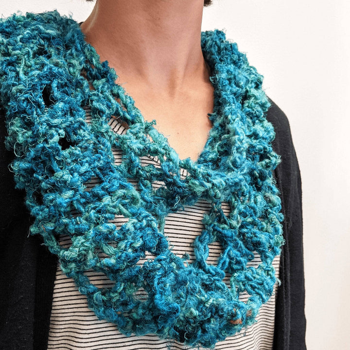Model wearing rainy day infinity knit scarf in blue with striped top and black cardigan in front of a white background.