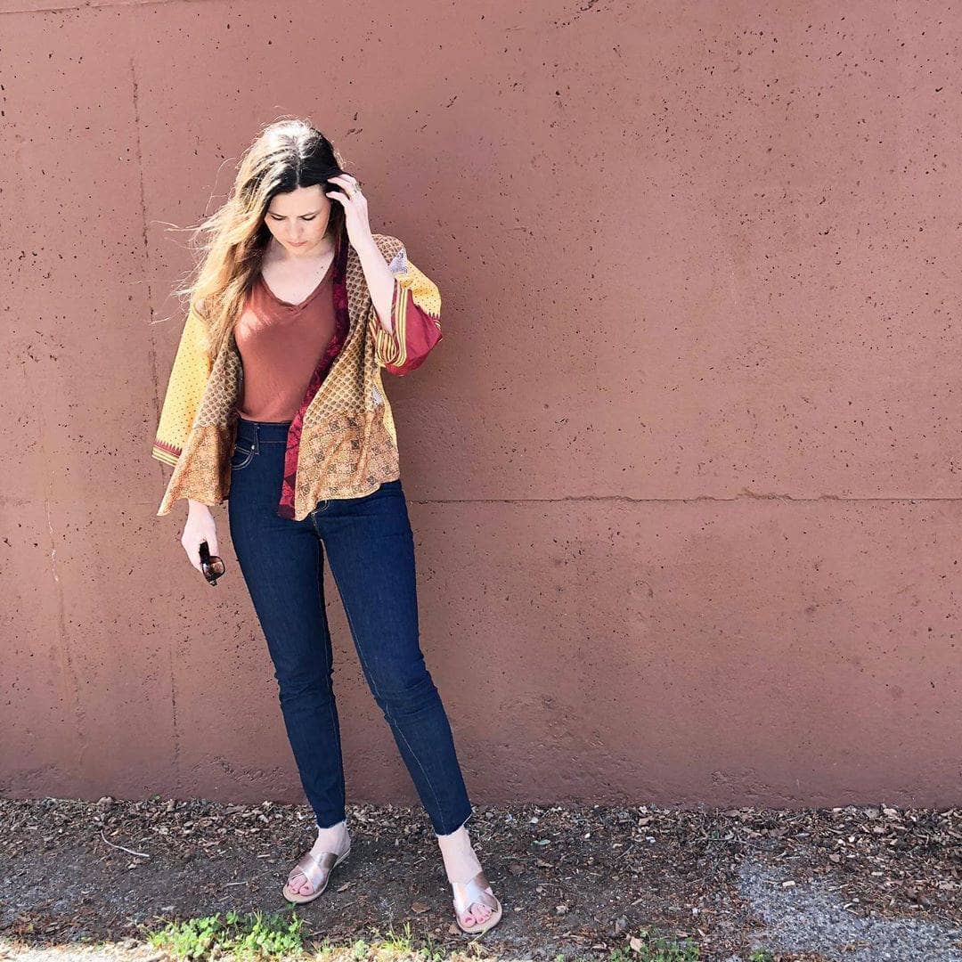 girl looking down and wearing a sari silk fabric jacket with a brown wall behind her