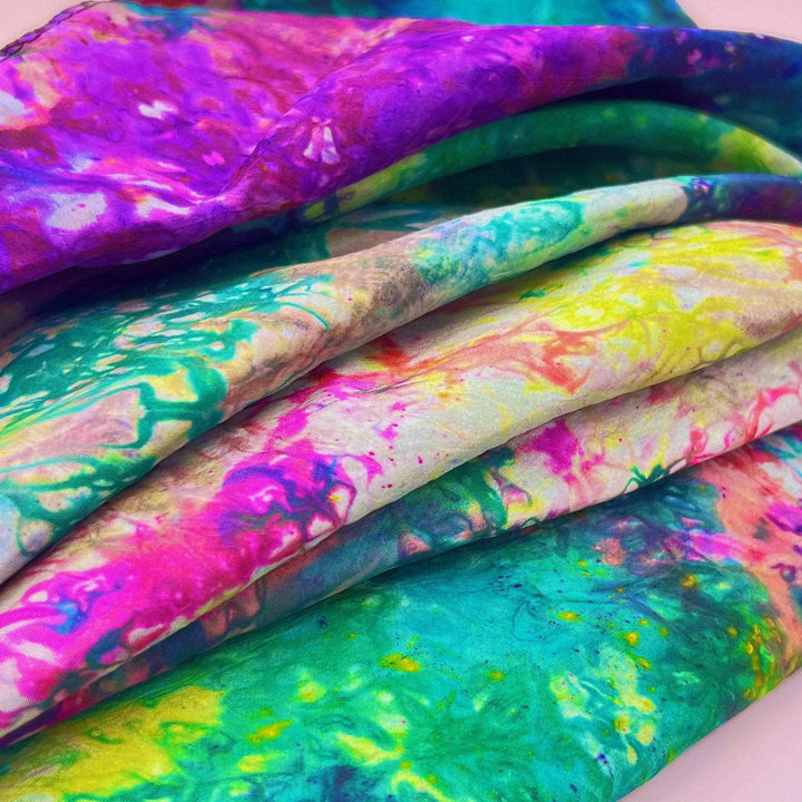 Folded fabric in vibrant tie-dye colors of purple, green, and yellow.