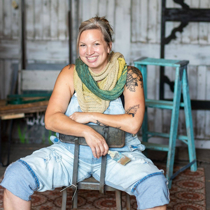 Model wearing ripple in the sand shawl while sitting backwards in a chair with a barn wall in the background.