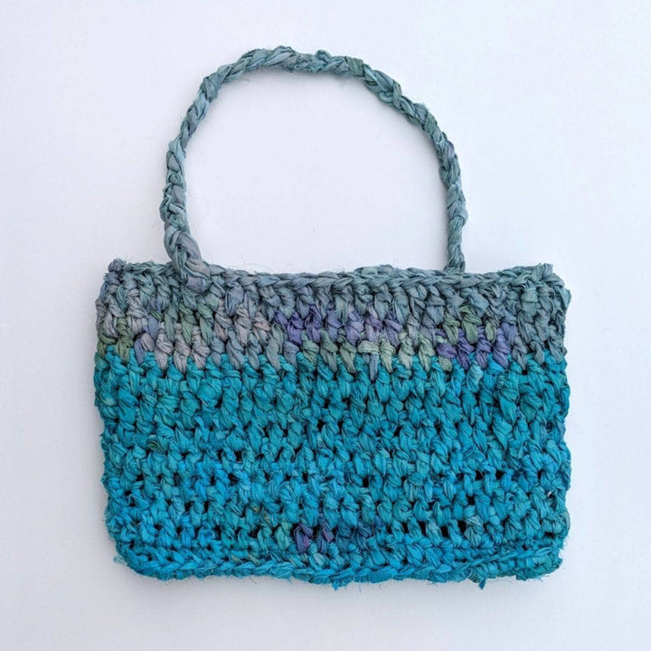 A blue and gray purse laying flat on a white background 