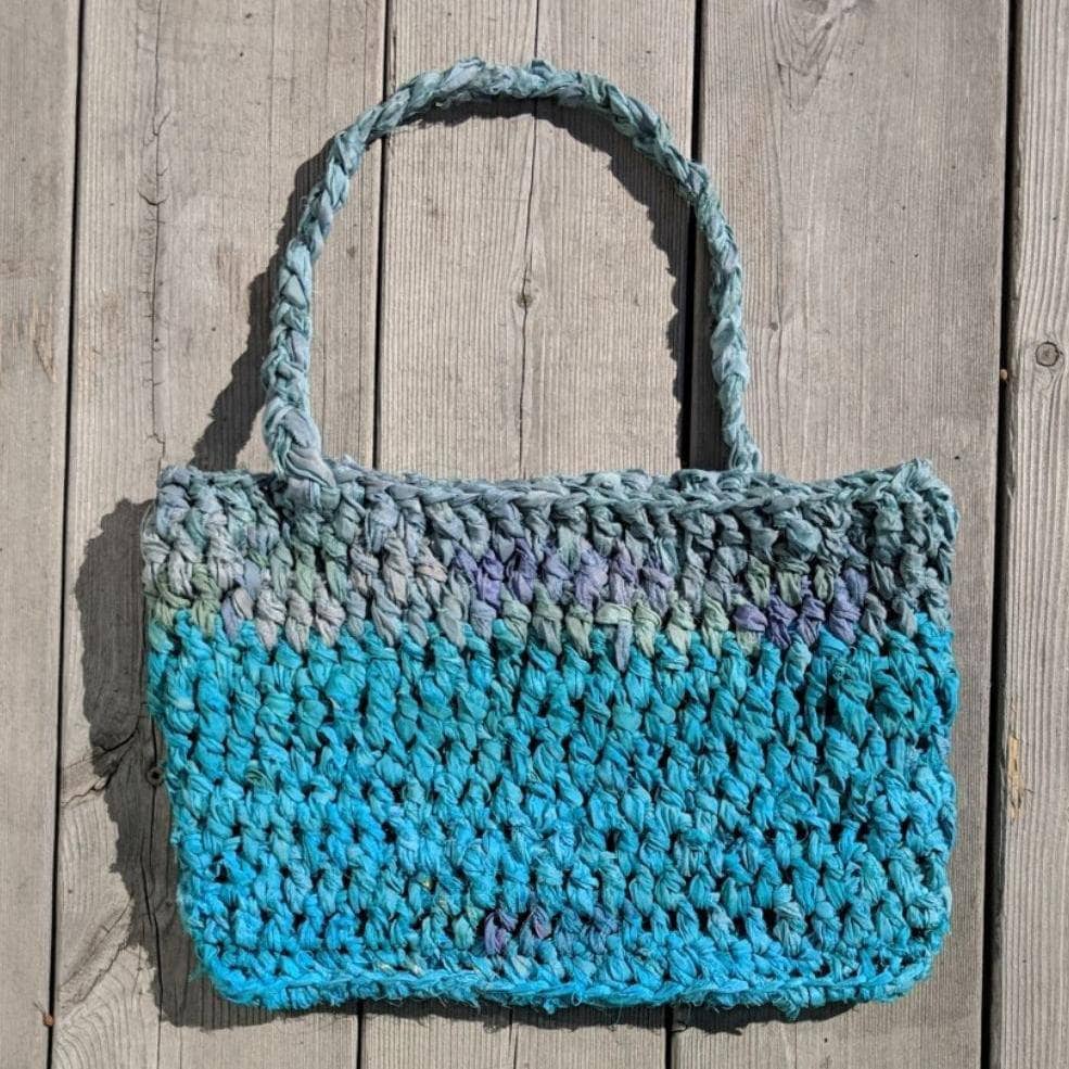 A blue and gray purse laying flat on a wooden background 