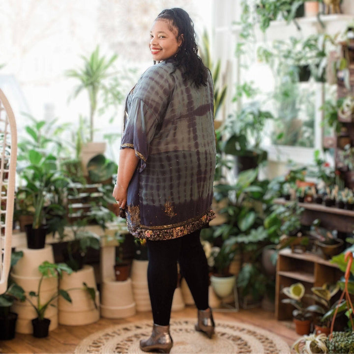 A woman turning her back smiling wearing short amara duster with plants in the background.