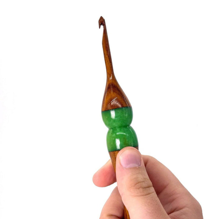 A hand holing a  wooden and resin crochet hooks.