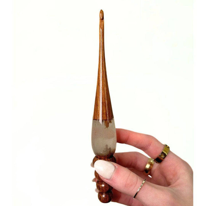 A woman's hand holing a  wooden and resin crochet hooks.