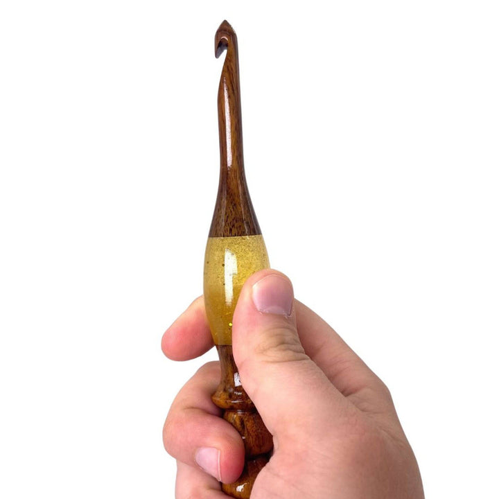 A hand holing a  wooden and resin crochet hooks.