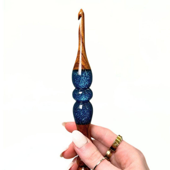 A woman's hand holing a  wooden and resin crochet hooks.