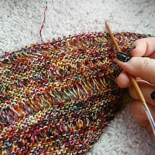In progress picture of a red and yellow speckled shawl with a yarn bowl in the top of the picture on a white background
