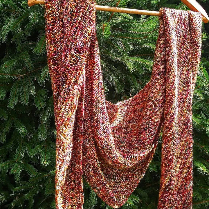 A specked red and yellow shawl hanging on a hanger on a tree