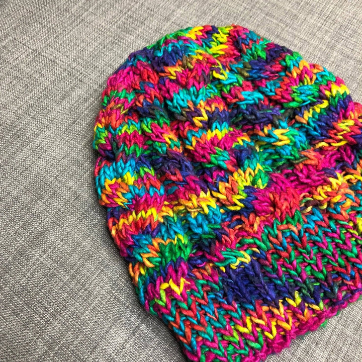 A colorful  Magnolia Beanie laying on a grey couch. 
