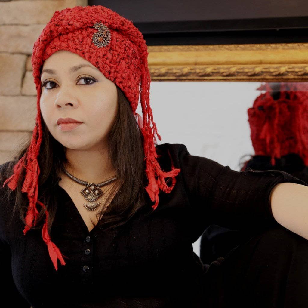 Woman wearing The Red Taj Headscarf in Paisley Red and standing in front of brick 