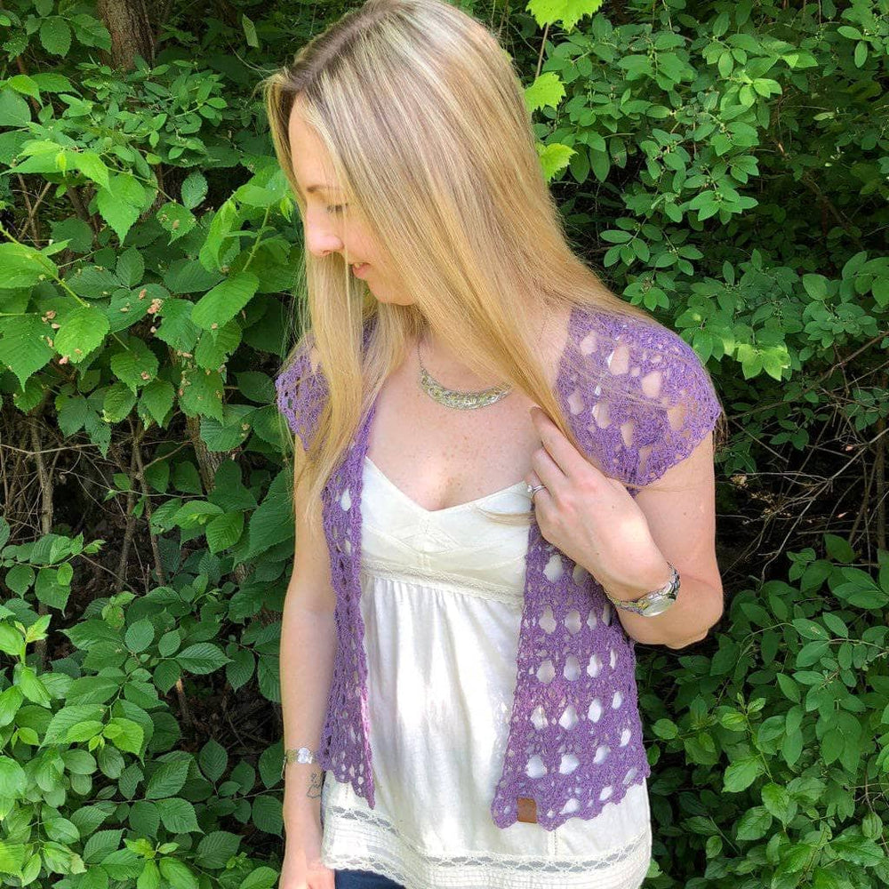 Woman wearing The Shenandoah Shrug in Purple standing in front of greenery
