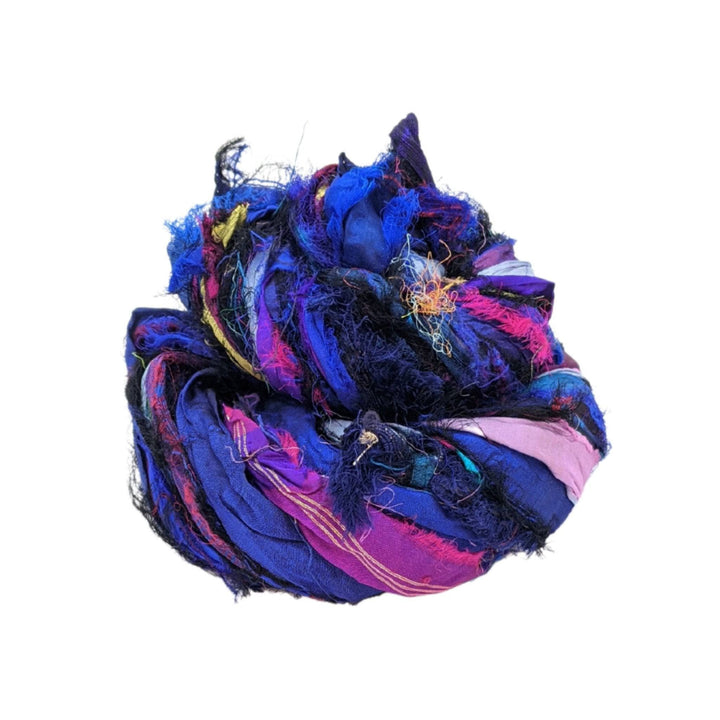 Skein of windswept sari silk ribbon yarn indigo in front of a white background. 
