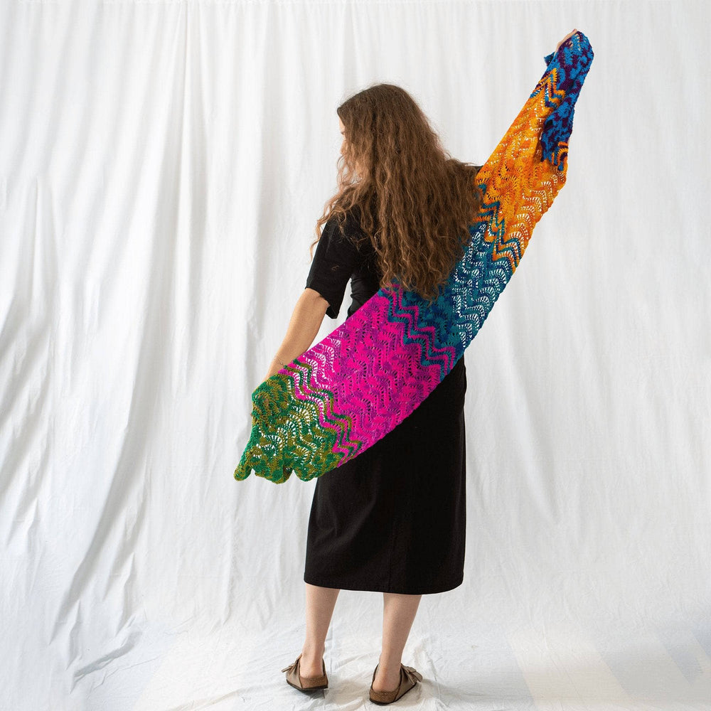 A woman standing facing at the back holding a colorful crochet scarf.
