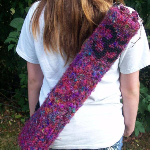 Yoga Mat Carrying Bag crocheted in pink yarn with black om symbol held across woman's back