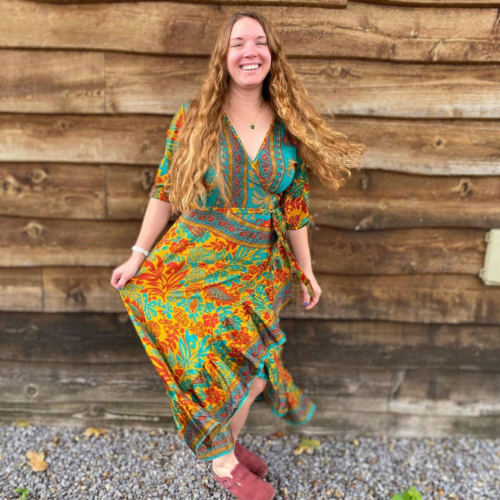 Smiling woman in a bright patterned dress, standing against a wooden wall