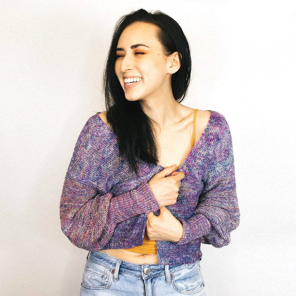 Woman wearing Zephyr Tides Cardi in Tidal Pool (purple) against a white wall