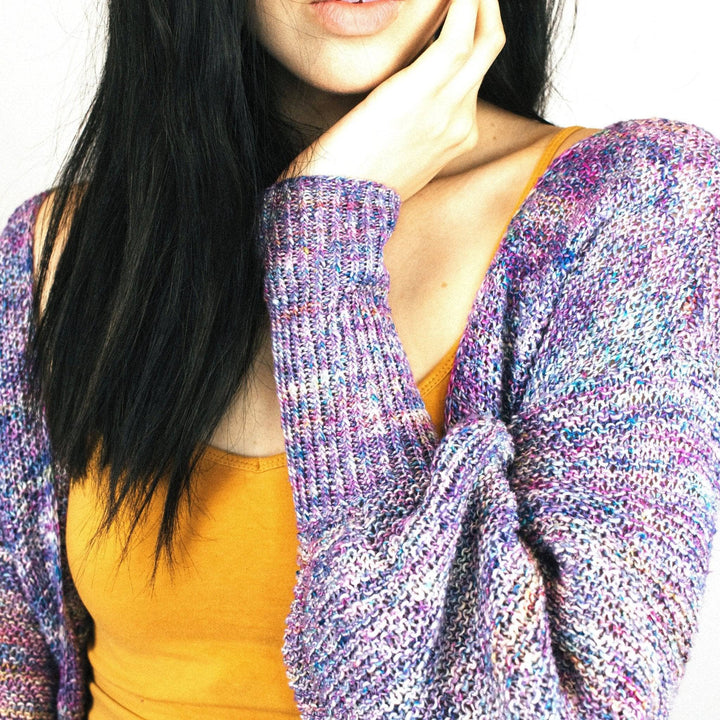 Close up of woman wearing Zephyr Tides Cardi in Tidal Pool (purple) against a white wall