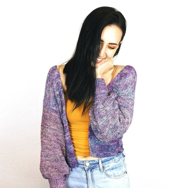 Woman wearing Zephyr Tides Cardi in Tidal Pool (purple) against a white wall