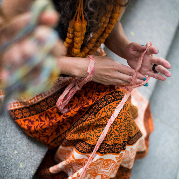 Model wearing orange cotton wrap skirt while arm knitting and sitting on concrete steps.