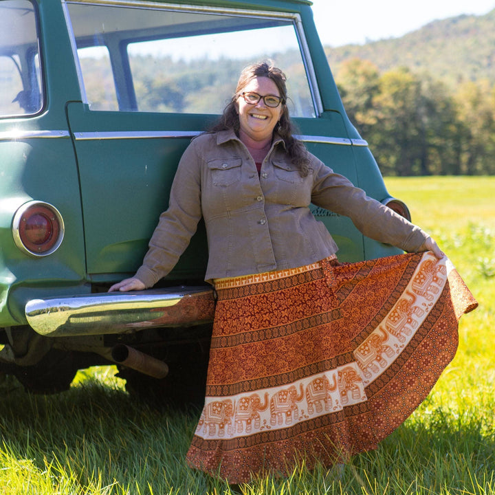 Model is standing outside in front of an old green truck wearing an orange cotton wrap around skirt. 